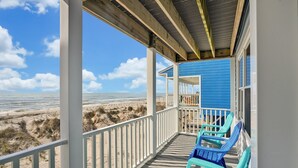 Une maison de plage dotée d’un porche couvert, d’une façade bleue et offrant une vue sur la plage.