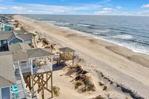 A beachside property with a wooden deck, a lifeguard tower, and a view of the ocean. - Experience oceanfront luxury at Dragonfly in Oak Island, sleeping up to 12 guests. (Oak Island)