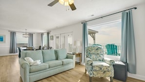 Un salon spacieux avec un canapé vert clair, un fauteuil à motifs floraux et un plancher en bois.
