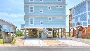 Una casa frente al mar de varios pisos con un porche cubierto y terraza de madera.