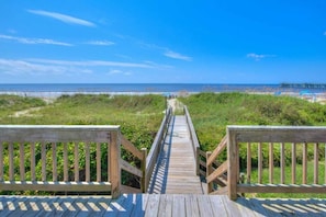 A wooden boardwalk leading to a beach with a pier in the distance.