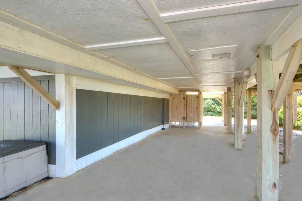Un espace extérieur abrité, doté d’un sol en béton, de piliers en bois et d’un mur gris.