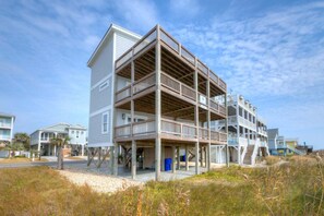 A multi-story beachfront building with balconies, a covered lower level, and a sandy foreground. - Experience beachfront luxury at Fishizzle in Oak Island, perfect for family getaways. (Oak Island)