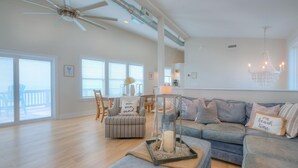 Un salón amplio con un gran ventanal, ventilador de techo, un conjunto de sofás y un comedor.