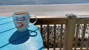 Vista a la playa con una terraza de madera y una mesa con una taza de café.