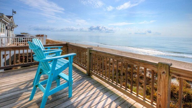 Una terraza de madera con barandilla que da a una playa.