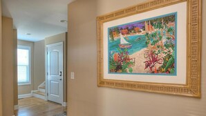 A hallway with a framed painting of a beach scene, a white door, and a staircase. - Discover Gypsea, a spacious 4-bedroom oceanview home in Oak Island, perfect for 10 guests! (Oak Island)