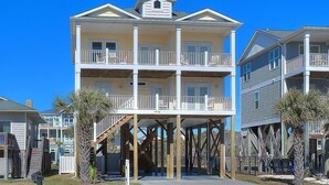 A multi-story beachfront building with balconies, wooden support beams, and a clear blue sky. - Discover Gypsea, a spacious 4-bedroom oceanview home in Oak Island, perfect for 10 guests! (Oak Island)