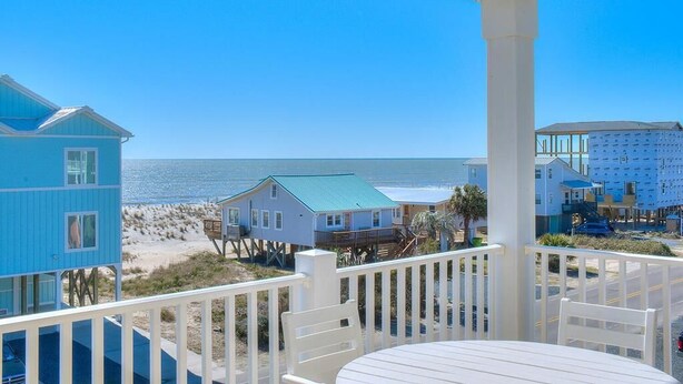 A beachfront property with a balcony overlooking the ocean, featuring a dining area with white furniture and a view of the beach and ocean. - Discover Gypsea, a spacious 4-bedroom oceanview home in Oak Island, perfect for 10 guests! (Oak Island)