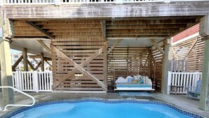 Ein Poolbereich mit Holzterrasse, einer Hängeschaukel und einem weißen Zaun.
