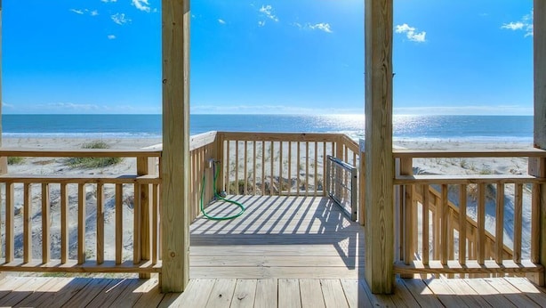 Una terraza de madera con vista a la playa y al océano.