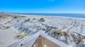 Una playa arenosa con una terraza de madera y un cielo azul despejado.