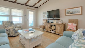 Una sala de estar con televisión, un ventanal grande, un sofá y una silla.
