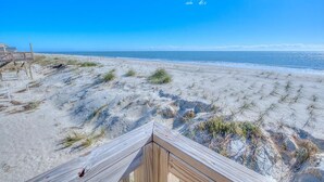 Une plage de sable avec une terrasse en bois et un ciel bleu dégagé.