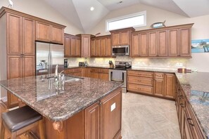 A kitchen with wooden cabinets, granite countertops, stainless steel appliances, and a large island with seating.