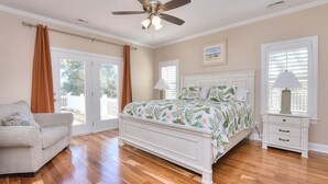 Une chambre à coucher avec un lit, un ventilateur de plafond, une table de chevet et une fenêtre avec des stores.