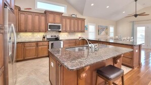 Une cuisine spacieuse avec des meubles en bois, un îlot central doté d’un comptoir en granit, des appareils électroménagers en acier inoxydable et une grande fenêtre.