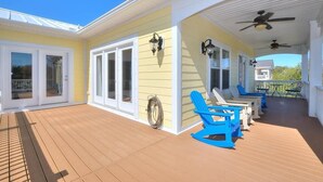 Une terrasse extérieure couverte, dotée de portes-fenêtres coulissantes, de chaises Adirondack bleues et de ventilateurs de plafond.