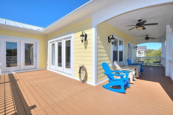 A covered outdoor deck with sliding glass doors, blue Adirondack chairs, and ceiling fans.