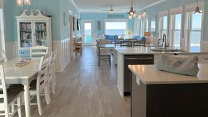Uma cozinha espaçosa com uma ilha grande, uma área de refeições com mobiliário branco e vista para o oceano através de amplas janelas.