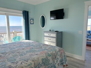 A bedroom with a bed, a dresser, a TV, and a view of the ocean.