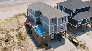 Um imóvel à beira-mar com piscina, várias varandas e um deck de madeira com cadeiras.