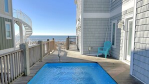 Um deck de madeira com piscina, uma cadeira e vista para o oceano.
