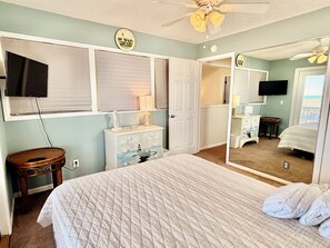 Une chambre à coucher comprenant un lit, une commode, un miroir et un ventilateur de plafond.