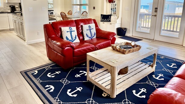 Een woonkamer met een rode leren bank, een houten bijzettafeltje en een vloerkleed met ankerprint.