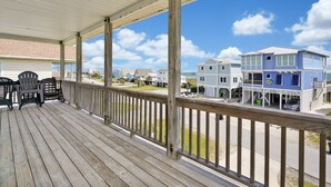 A wooden deck with chairs, a covered area, and a view of houses. - Experience ocean views at Oak Island's 4-bedroom Kelly Dawn, perfect for 10 guests! (Oak Island)