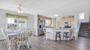 A modern kitchen with a central island, wooden dining table with chairs, and a staircase leading to an upper level. - Experience ocean views at Oak Island's 4-bedroom Kelly Dawn, perfect for 10 guests! (Oak Island)