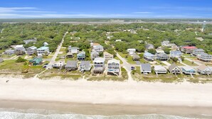 An aerial view of a coastal residential area with houses, a beach, and a bridge in the distance. - Experience ocean views at Oak Island's 4-bedroom Kelly Dawn, perfect for 10 guests! (Oak Island)