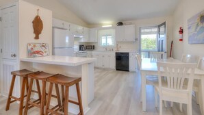 A modern kitchen with white cabinetry, a central island with stools, and a dining area with white chairs.