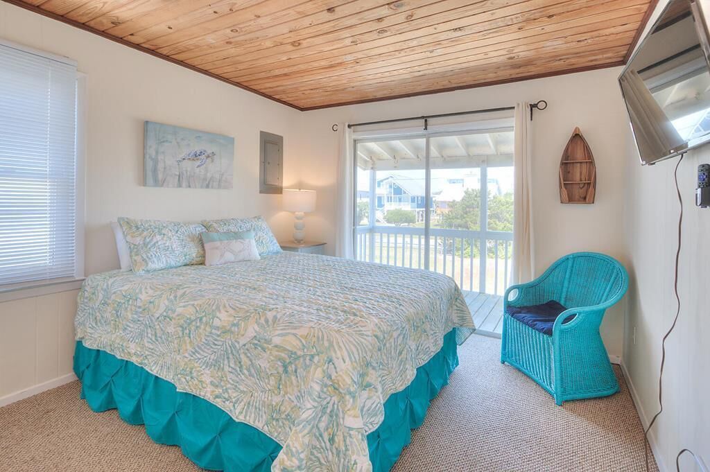 A bedroom with a bed, a window, a painting, a chair, and a balcony.