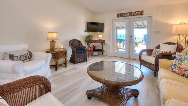 A beach-themed living room with wicker furniture, a glass-top table, and a television.