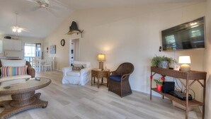 A spacious living room with a flat-screen TV, wicker furniture, and a ceiling fan.