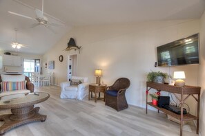 A spacious living room with a flat-screen TV, wicker furniture, and a ceiling fan.