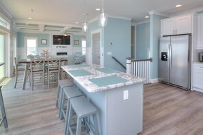 A kitchen with a central island, bar stools, a refrigerator, and a dining area with chairs and a table.