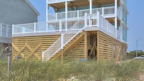 A multi-story building with a wooden deck and a staircase leading to the upper levels. - Experience luxury in this oceanfront 5-bedroom retreat in Oak Island. (Oak Island)