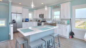 A modern kitchen with white cabinets, a large island with bar stools, stainless steel appliances, and pendant lighting. - Experience luxury in this oceanfront 5-bedroom retreat in Oak Island. (Oak Island)