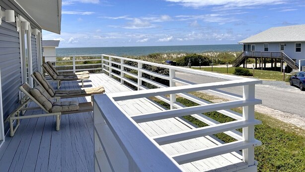 Eine Holzterrasse mit Liegestühlen, einem weißen Geländer und Blick auf das Meer.