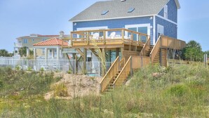 A two-story house with a wooden deck and stairs leading to a balcony. - Oceanfront Monkeytyme in Oak Island: 5BR, 4BA, sleeps 13, perfect for families! (Oak Island)