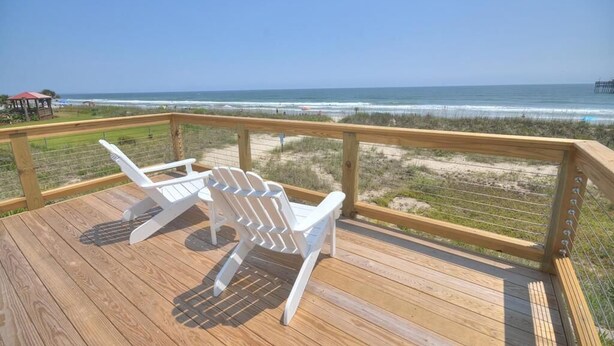 A wooden deck with two white Adirondack chairs facing a beach. - Oceanfront Monkeytyme in Oak Island: 5BR, 4BA, sleeps 13, perfect for families! (Oak Island)