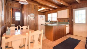 A wooden cabin interior with a dining table and chairs, a kitchen area with a refrigerator, and a door with a window. - Experience beach living at Morning Star, a charming 3-bedroom home in Oak Island! (Oak Island)
