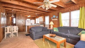 A cozy cabin-style room with a striped sofa, a wooden coffee table, and a ceiling fan. - Experience beach living at Morning Star, a charming 3-bedroom home in Oak Island! (Oak Island)