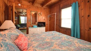 A wooden-paneled room with a bed, a dresser, a television, and a window with curtains. - Experience beach living at Morning Star, a charming 3-bedroom home in Oak Island! (Oak Island)