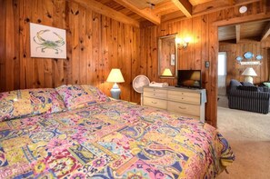 Una habitación con paneles de madera, una cama, un aparador, un televisor y un espejo.