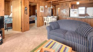A cozy cabin-style room with a striped sofa, a dining table, and a kitchen area. - Experience beach living at Morning Star, a charming 3-bedroom home in Oak Island! (Oak Island)