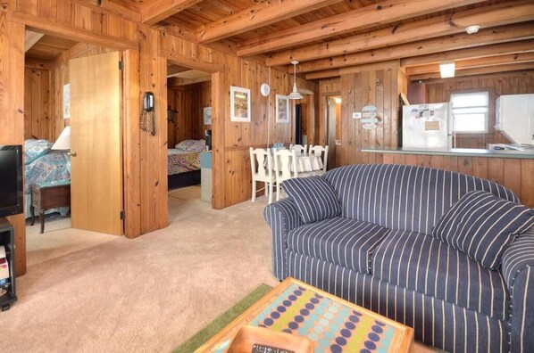 A cozy cabin-style room with a striped sofa, a dining table, and a kitchen area.