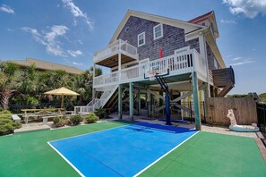 Ein zweistöckiges Gebäude mit Basketballplatz, Sitzgelegenheiten im Freien und einer Holzterrasse.